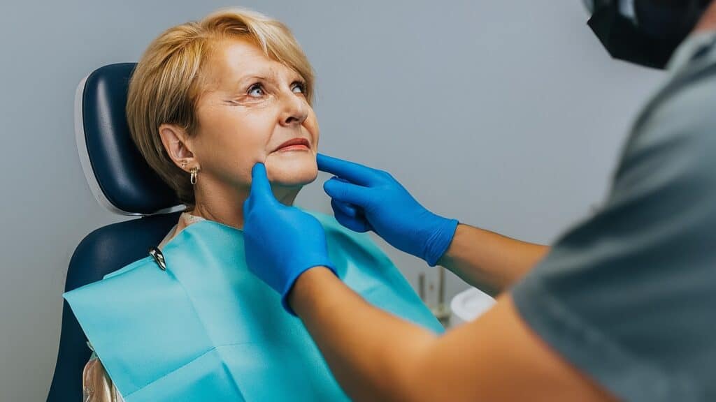 An image of a woman sitting in a dental chair while her dentist examines her jaw for TMJ.